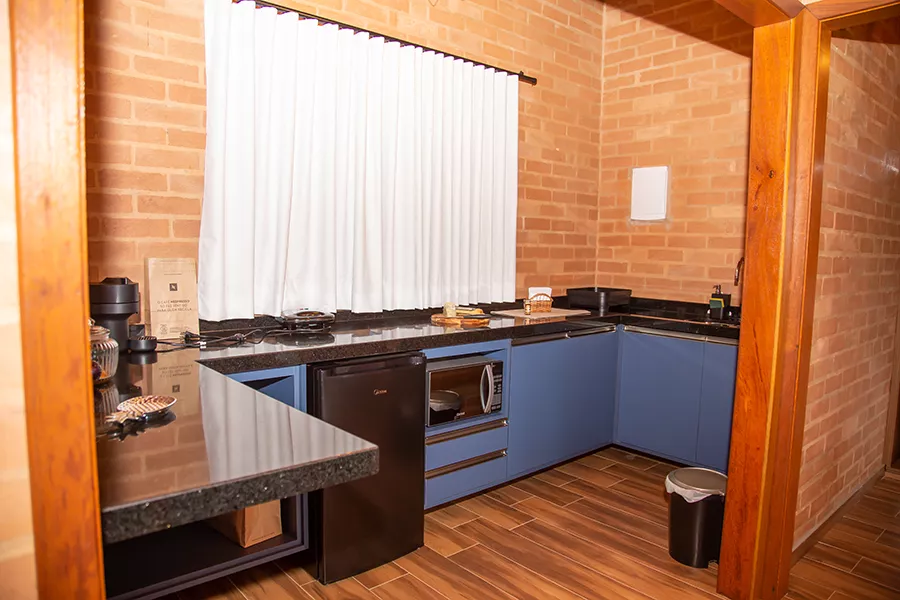 Modern kitchen with blue cabinets, black countertop, small black refrigerator, microwave, and window with white curtains.